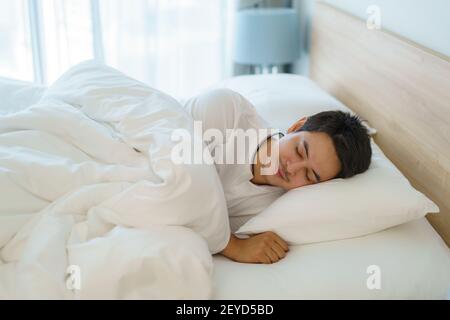 L'uomo asiatico sta dormendo e ha buoni sogni in coperta bianca la mattina. Riposo dopo il lavoro faticoso in camera da letto a casa Foto Stock