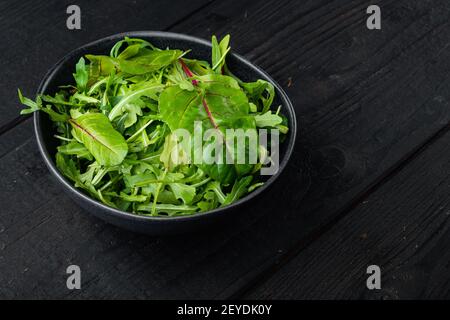 Verde misto fresco crudo Arugula raab, Mangold, Set bietole svizzero, su sfondo nero tavola di legno, con spazio copia per il testo Foto Stock