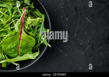 Insalata verde di erbe con rucola e mangold, set bietole svizzero, su fondo di pietra nera, vista dall'alto piatto, con spazio per la copia del testo Foto Stock