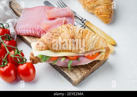 Panino di croissant con prosciutto, pomodori, set di formaggi, con erbe e ingredienti, su fondo di pietra bianca Foto Stock