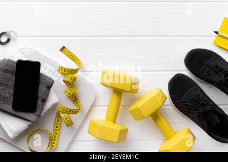 Flat lay top view attrezzature sportive, sneakers e smartphone su sfondo bianco in legno. Programma di fitness personale concetto di allenamento Foto Stock