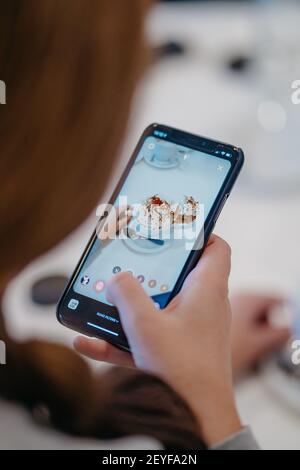 Una mano femminile con il telefono cellulare che scattano foto di il caffè è decorato con panna montata Foto Stock