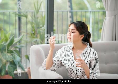 Donna felice di prendere una vitamina giallo pillola seduta su un divano nel salotto di casa Foto Stock