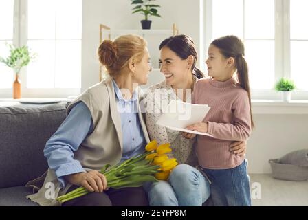 Signora anziana che ottiene i fiori dalla figlia amorevole e dalla nipote sopra Festa della mamma Foto Stock