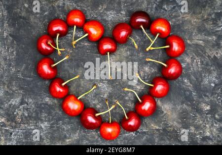 Ciliegie dolci rosse mature disposte a forma di grande cuore su un tavolo grugnoso. Concetto d'amore romantico. Foto Stock