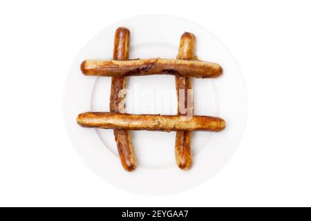 Primo piano di un simbolo di hash fatto di tradizionali salsicce di carne di maiale alla griglia su un grande piatto bianco isolato su sfondo bianco. Foto Stock