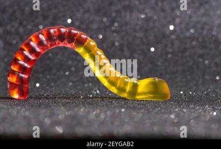 Primo piano di un verme gommoso rosso-giallo retroilluminato strisciato su uno sfondo scintillante. Foto Stock