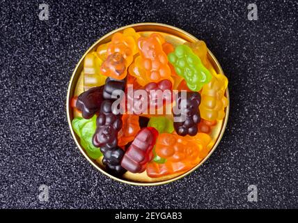 Vista dall'alto di un mucchio di orsi gommoso multicolore su un coperchio di latta contro sfondo nero. Foto Stock