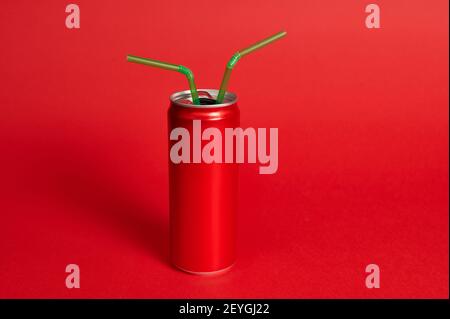 Studio girato con una morbida ombra di una lattine di metallo rosso con due cannucce verdi su sfondo rosso. Verde-rosso, contrasto del colore Foto Stock