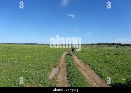 Un adolescente che guida una mountain bike elettrica in un paese remoto traccia Foto Stock