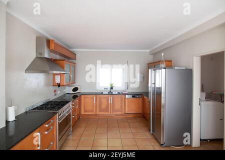 Cucina grande ma antiquata con armadietti di legno e bancone di granito in alto Foto Stock