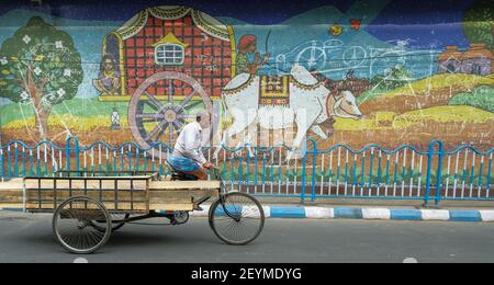 Kolkata, India - 2021 febbraio: Un uomo in bicicletta che passa un mosaico di un carro trainato da una mucca il 3 febbraio 2021 a Kolkata, Bengala Occidentale, India. Foto Stock