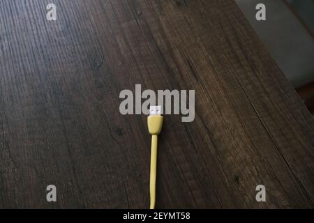 Cavo USB di colore giallo che si trova su un tavolo di legno scuro. Foto Stock