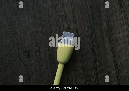 Cavo USB di colore giallo che si trova su un tavolo di legno scuro. Foto Stock