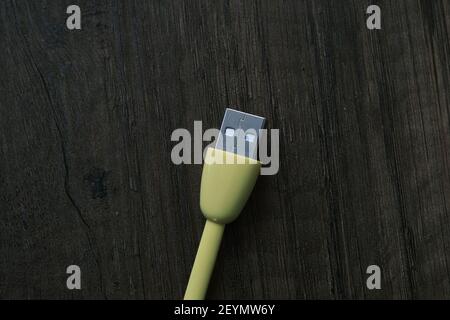 Cavo USB di colore giallo che si trova su un tavolo di legno scuro. Foto Stock