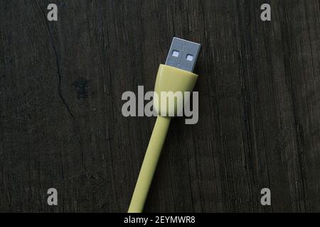 Cavo USB di colore giallo che si trova su un tavolo di legno scuro. Foto Stock