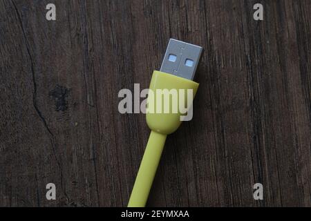 Cavo USB di colore giallo che si trova su un tavolo di legno scuro. Foto Stock