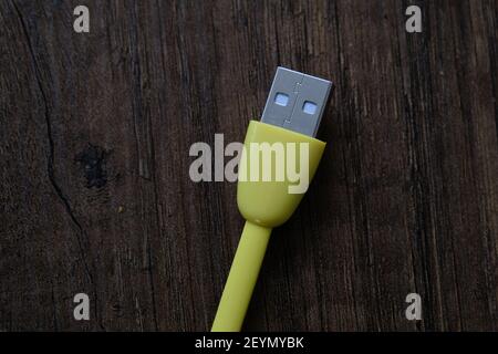 Cavo USB di colore giallo che si trova su un tavolo di legno scuro. Foto Stock