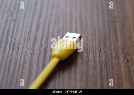 Cavo USB di colore giallo che si trova su un tavolo di legno scuro. Foto Stock