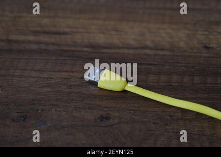Cavo USB di colore giallo che si trova su un tavolo di legno scuro. Foto Stock
