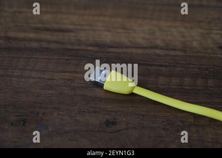 Cavo USB di colore giallo che si trova su un tavolo di legno scuro. Foto Stock