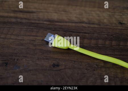 Cavo USB di colore giallo che si trova su un tavolo di legno scuro. Foto Stock