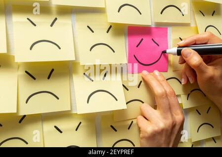 Un segno di un sorriso disegnato su un adesivo su uno sfondo di volti tristi di icone. Simbolo di successo aziendale. Foto Stock