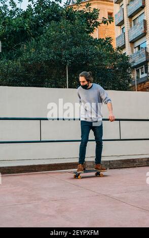 Immagine di Vertical Shot di Male Skater con maschera nera Skateboarding in una pista del Parco. Foto Stock