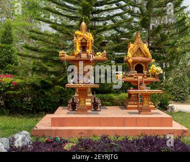 Altare con offerte a Budha in Thailandia, vista dal fronte, con piante in primo piano e sullo sfondo, che suggerisce un giardino Foto Stock