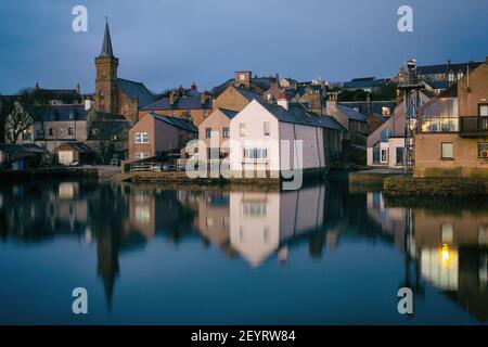 Vista dal lato dell'acqua delle case scozzesi sulle isole Orcadi con edifici riflessi in acqua al mattino Foto Stock