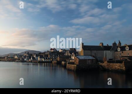 Vista sul lungomare della città scozzese sulle isole Orkney con vintage case nuvole bianche su cielo blu al mattino Foto Stock