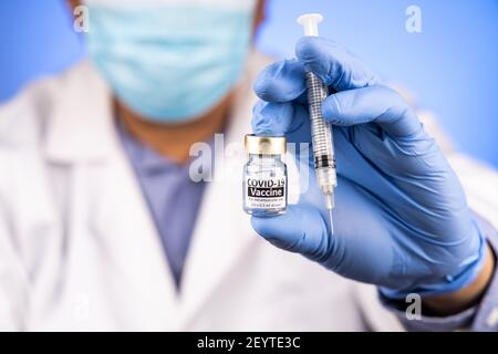 Primo piano e attenzione al flaconcino di vaccino Covid-19 e alla siringa contenuta Da medico asiatico con guanto medico in background Foto Stock