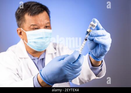 Primo piano e concentrazione sulla siringa inserita nel flaconcino del vaccino Covid-19 Da medico asiatico con guanto medico in background Foto Stock