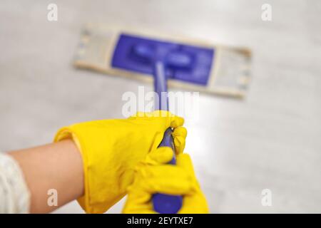 Giovane donna in guanti protettivi di gomma gialla con mop bagnato piatto durante la pulizia del pavimento in casa. Foto Stock