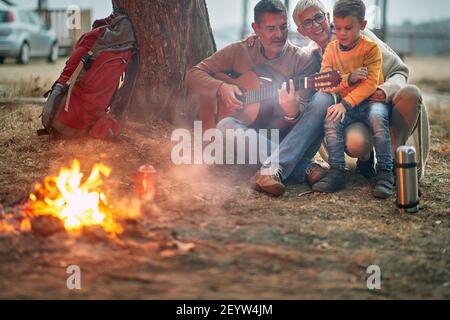 Felice nonni con ragazzo che suona la chitarra al picnic Foto Stock