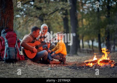 Bambino maschile con nonni al picnic suonando la chitarra Foto Stock