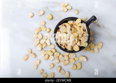 Fagioli secchi senza guscio in tazza nera su marmo bianco. Fagiolo Fava. Foto Stock