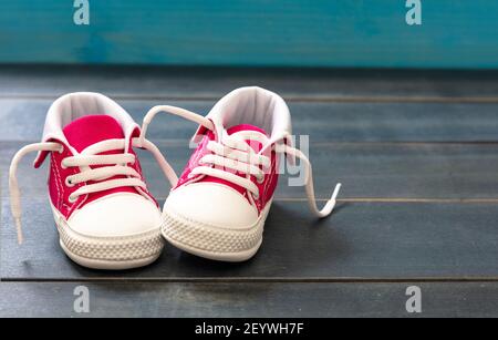 Scarpe sportive baby girl su pavimento in legno di colore blu. Scarpe da ginnastica rosa per bambini di piccole dimensioni, vista in primo piano con stivaletti in tela. Spazio, modello invito scheda Foto Stock