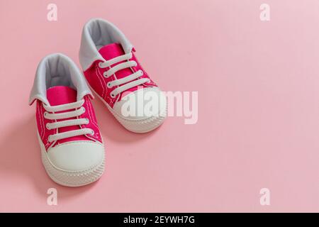 La sua una ragazza, Baby scarpe sportive su sfondo color rosa pastello. Scarpe da ginnastica per bambini di piccole dimensioni, vista in primo piano su stivaletti in tela. Spazio, modello invito scheda Foto Stock