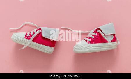 Baby girl sport scarpe camminare su sfondo di colore rosa pastello. Scarpe da ginnastica per bambini di piccole dimensioni, stivaletti in tela. I primi passi della ragazza. Foto Stock