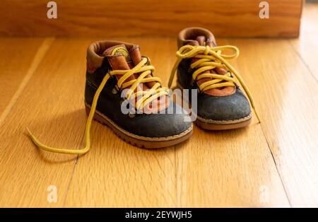 Vista guardaroba delle stivalette di piccole dimensioni per bambini. Scarpe per bambini in pelle di colore blu con lacci per scarpe gialli slegati su pavimento in legno. Camera per bambini Foto Stock