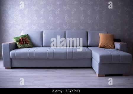 divano ad angolo grigio con cuscini sullo sfondo della parete Foto Stock