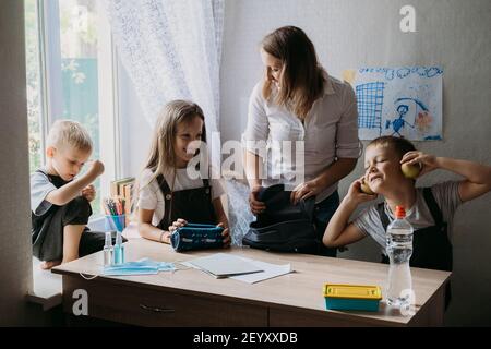 Torna a scuola in una nuova normalità. La madre aiuta i bambini a portare i loro zaini a scuola e dà loro maschere facciali e disinfettanti. Maschera medica a. Foto Stock
