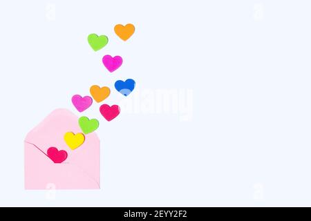 Cuori colorati che emergono da una busta rosa su uno sfondo blu chiaro. Spazio di copia per il testo Foto Stock