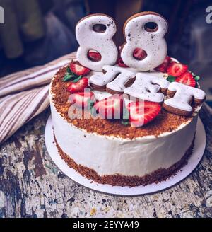 torta di compleanno fatta in casa con 88 anni scritto in russo su e fragole fresche Foto Stock