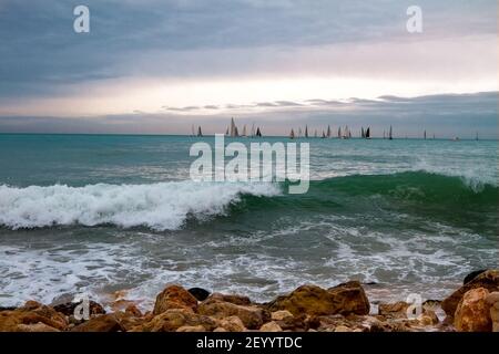 Grandi onde marine con spruzzi di schiuma e acqua sulla spiaggia e una regata di vela sullo sfondo dell'orizzonte. Foto Stock