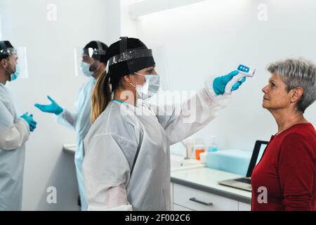 Medico che misura la temperatura con un nuovo termometro digitale per la paziente anziana durante la pandemia del virus corona Foto Stock