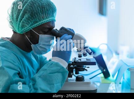 Scienziato che lavora in laboratorio esaminando il coronavirus attraverso il microscopio - Scienza e concetto di tecnologia Foto Stock