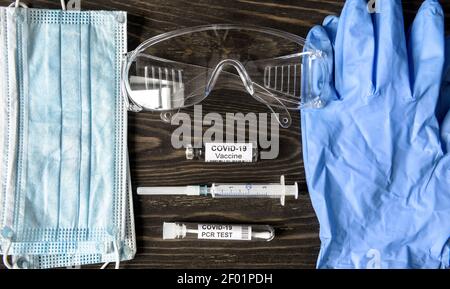 Kit medico COVID-19 coronavirus, vista dall'alto di apparecchiature personali (PPE), vaccino, siringa e test PCR. Composizione piatta di maschera protettiva, guanti Foto Stock