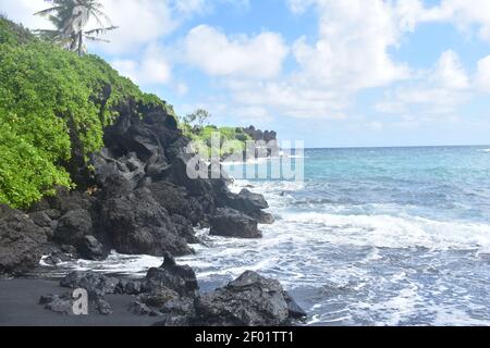 Il paesaggio di belle onde oceaniche che colpiscono le nere scogliere rocciose vulcaniche sullo sfondo dell'isola di Maui, Hawaii Foto Stock